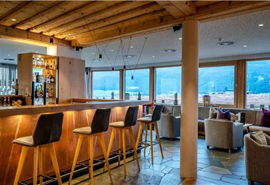 Eine moderne Bar mit Holzdekor und bequemen Sitzgelegenheiten. Große Fenster bieten Blick auf eine malerische Landschaft.