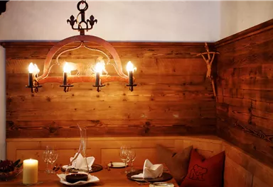 Ein gemütlicher Essbereich mit Holzwänden und einem eleganten Kronleuchter. Auf dem Tisch stehen weiße Servietten, Gläser und ein Kerzenständer.