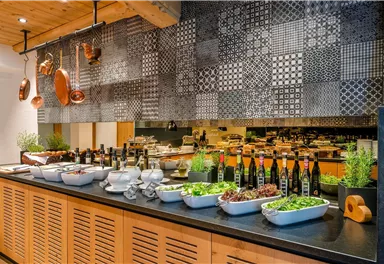 Ein eleganter Buffet-Bereich mit verschiedenen Frischen Zutaten und Ölen. An der Wand sind dekorative Muster zu sehen, die eine ansprechende Atmosphäre schaffen.