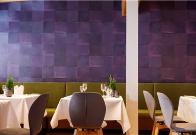 Ein stilvolles Restaurant mit eleganten Tischen und modernen Stühlen. Die Wände sind in einem schönen lila Farbton gestaltet.