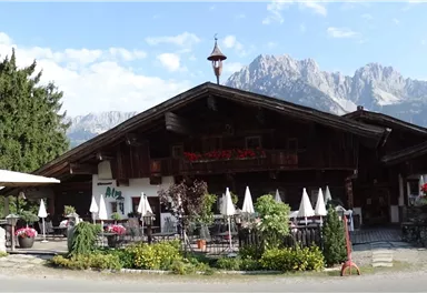 Ein traditionelles Alpenhaus mit einem schönen Garten und Terrassen. Im Hintergrund sind majestätische Berge zu sehen.