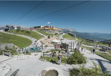 Ein malerischer Bergort mit vielen Besuchern und klar blauem Himmel. Die Umgebung ist grün und einladend, ideal für Outdoor-Aktivitäten.