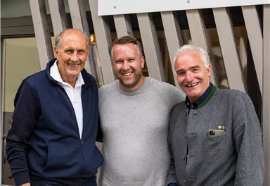 Drei Männer posieren vor dem Schild "Hair Lodge" in Ellmau. Die Stimmung ist freundlich und die Umgebung wirkt einladend.