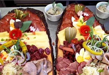 A lavish cold buffet with various types of meat, cheese, and fresh vegetables. There are decorative sides such as cucumbers, radishes, and herbs.