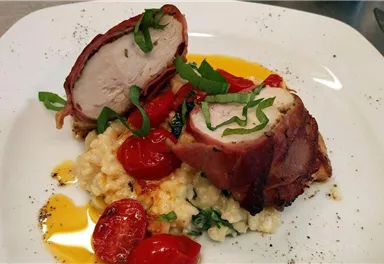 A decorative plate with stuffed chicken breast wrapped in bacon. Served with cherry tomatoes and a creamy side dish.