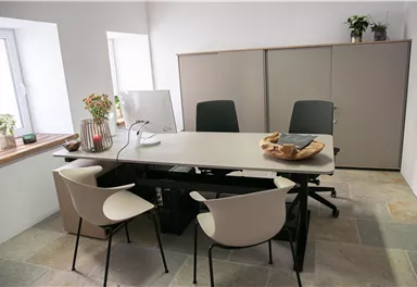 Ein modernes Büro mit einem großen Tisch und zwei Stühlen. Es gibt Pflanzen und eine helle, freundliche Atmosphäre.