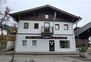 Ein zweigeschossiges Gebäude mit einem großen Schild, das "EVENTS" zeigt. Das Haus hat Fenster im oberen und unteren Bereich und befindet sich an einer Straßenkreuzung.