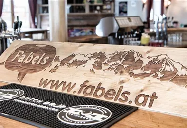 A wooden counter with the inscription "Fabels" and a mountain landscape. The website www.fabels.at is also visible.