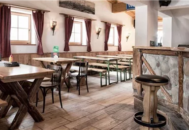 A cozy restaurant with wooden tables and benches. The atmosphere is inviting, with red curtains and warm light.