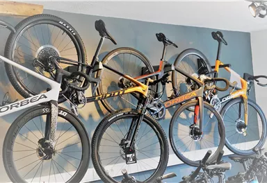 Three bicycles from the brand Orbea are hanging on a wall. They are designed in different colors and styles.