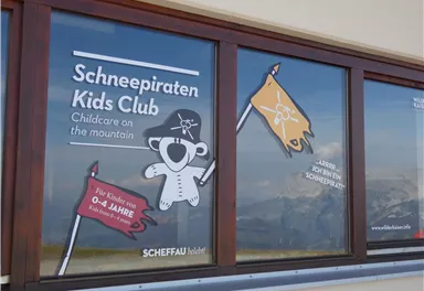 Ein Fenster mit einer Anzeige für den "Schneepiraten Kids Club". Es bietet Kinderbetreuung in den Bergen für Kinder von 0 bis 14 Jahren an.
