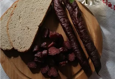 A wooden board with fresh bread and sliced cold cuts. Next to it is a towel with a red pattern.