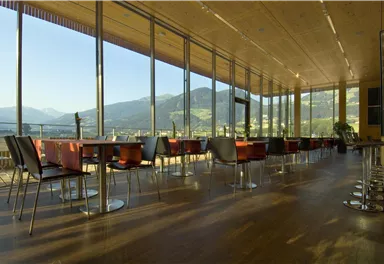 Ein modernes Restaurant mit großen Fenstern und Blick auf die Berge. Die Einrichtung ist minimalistisch und einladend.