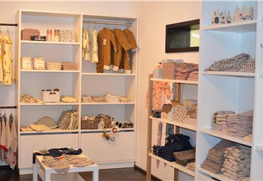Ein gemütlicher Laden mit Regalen voller Babybekleidung und Accessoires. Die Produkte sind ordentlich präsentiert und in sanften Farben gehalten.