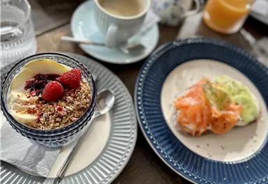 Ein gedeckter Tisch mit verschiedenen Frühstücksgerichten. Im Vordergrund ein Joghurt mit Beeren und einem Snack aus Lachs und Gemüse.