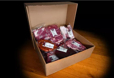 An open cardboard box with various meat packages. The packages are labeled and contain different types of meat.