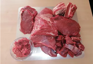 A selection of various cuts of meat is on a table. In a bowl, there is minced meat.