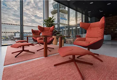 A modern room with red chairs and a table that receives plenty of daylight from large windows. In the background, an airport tower is visible.
