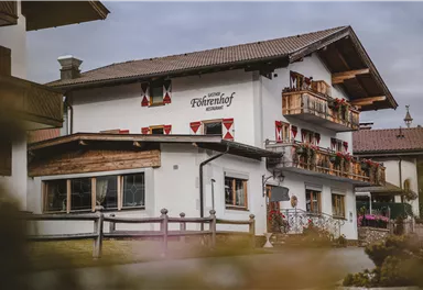 A traditional building with wooden cladding and a balcony. It is decorated in a quiet environment with beautiful flower boxes.
