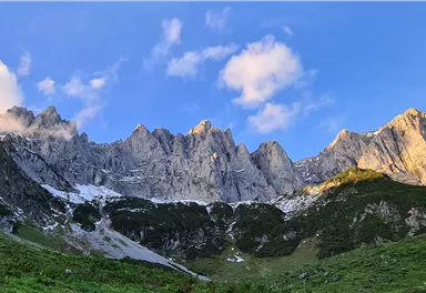 Eine beeindruckende Gebirgslandschaft mit hohen, schroffen Bergen. Der Himmel ist klar und blau, mit einigen weißen Wolken.