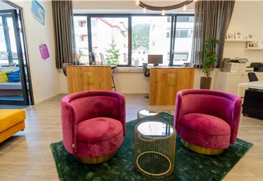 Ein modernes Büro mit zwei pinken Sessel und einem kleinen Tisch. Große Fenster bieten viel Tageslicht und einen Blick nach draußen.