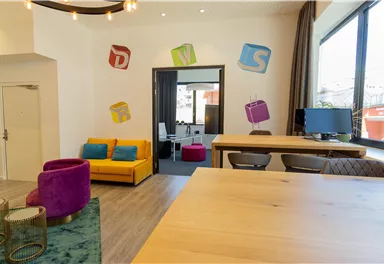 Ein modernes Büro mit bunten Wanddekorationen und gemütlichen Sitzgelegenheiten. Der Raum ist hell und einladend, ideal für kreative Arbeit.