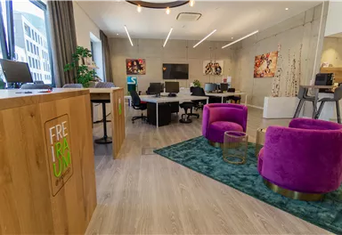 Ein modernes Büro mit hellen Farben und stilvollen Möbeln. Im Vordergrund sind zwei lila Sessel auf einem Teppich zu sehen.