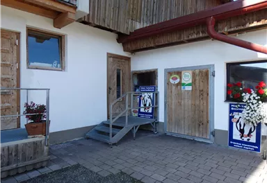 A building with wood siding and two doors. In front of the entrance stairs are plants and posters.