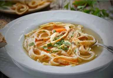 A delicious soup with pasta, carrots, and fresh herbs. Served in a white bowl on a rustic wooden background.