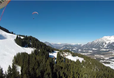 A clear blue sky over a beautiful mountain landscape with snow-covered slopes. In the background, impressive mountains and dense forests can be seen.
