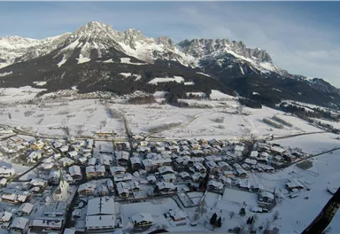 A snow-covered landscape with a small village and impressive mountains in the background. The calm winter atmosphere radiates peace.