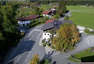 A picturesque village view with traditional houses and a quiet street. The surroundings are green and surrounded by trees.