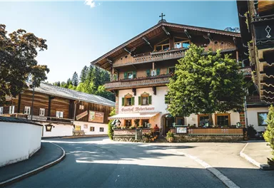 A traditional building in alpine style with a wooden-clad facade. Surrounded by trees and a clear blue sky.