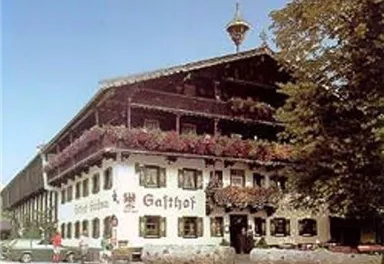 Ein traditionelles Gasthaus mit blühenden Blumenfenstern und einem rustikalen Dach. Die Umgebung ist grün und einladend.