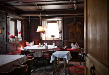 A cozy room with wooden walls and a table in the middle. Gentle light filters through the windows, creating an inviting atmosphere.