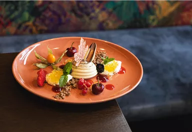 Ein schönes Dessert auf einem orangefarbenen Teller. Es besteht aus einer Creme, Früchten und einer dekorativen Essbarem.