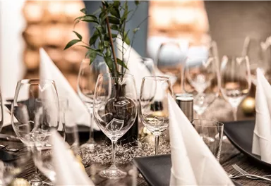Ein festlich gedeckter Tisch mit eleganten Gläsern und gefalteten Servietten. In der Mitte steht eine kleine Pflanze als Dekoration.