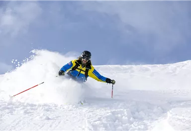 Ein Skifahrer fährt durch den frischen Schnee. Der Himmel ist klar und blau.