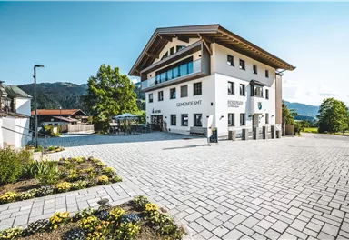 Ein modernes Gebäude mit einem klaren blauen Himmel im Hintergrund. Vor dem Gebäude befindet sich ein schön gestalteter Außenbereich mit Blumenbeeten.