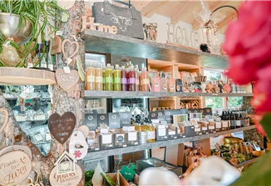 Ein gemütlicher Laden mit Regalen voller Naturprodukte und dekorativen Artikeln. Es gibt farbige Flaschen, Seifen und liebevolle Holzschilder zur Deko.