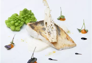 An artistically arranged fish with a crispy skin, garnished with Romanesco and colorful sauces. The dish is elegantly and appealingly presented.