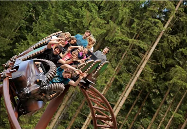 A roller coaster with happy passengers winds through a forest. The people are having fun and enjoying the ride in nature.