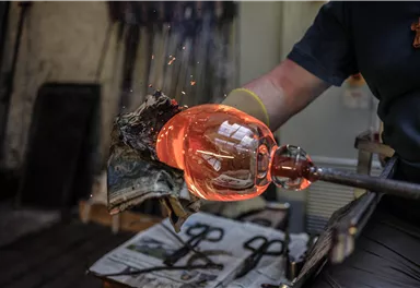 Ein Glasmacher formt einen heißen, glühenden Glasball. Funken sprühen, während er das Glas bearbeitet.