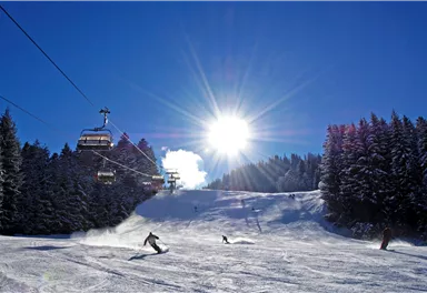 Ein sonniger Skitag in den Bergen. Skifahrer fahren die Pisten hinunter, umgeben von schneebedeckten Bäumen.