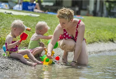 A mother plays with her two small children on the shore. They have toys and enjoy the water on a sunny day.