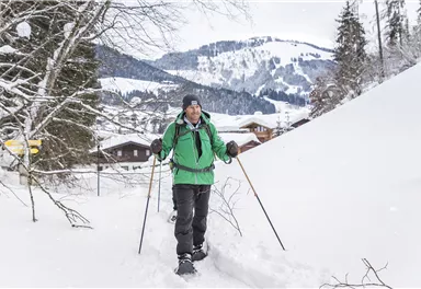 A man is snowshoeing through a snow-covered landscape. In the background, mountains and charming cottages can be seen.