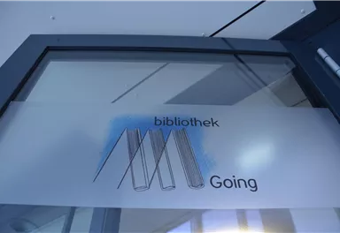 Ein Glasfenster mit der Aufschrift "bibliothek Going". Darauf sind stilisierte Bücher abgebildet.