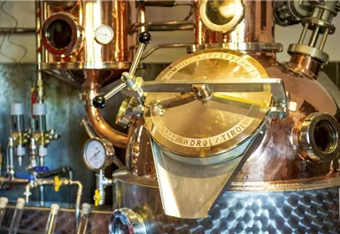 A copper still in a distillery. The apparatus has shiny surfaces and various instruments for control.