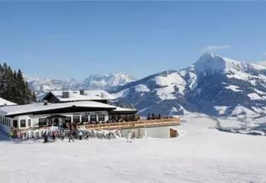 A cozy restaurant in the mountains, surrounded by snow-capped peaks. Skiers and visitors enjoy the view of the picturesque winter landscape.