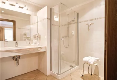 Ein modernes Badezimmer mit einer gläsernen Dusche und einem eleganten Waschtisch. Die Wände sind hell gefliest und das Raumdesign ist schlicht und einladend.